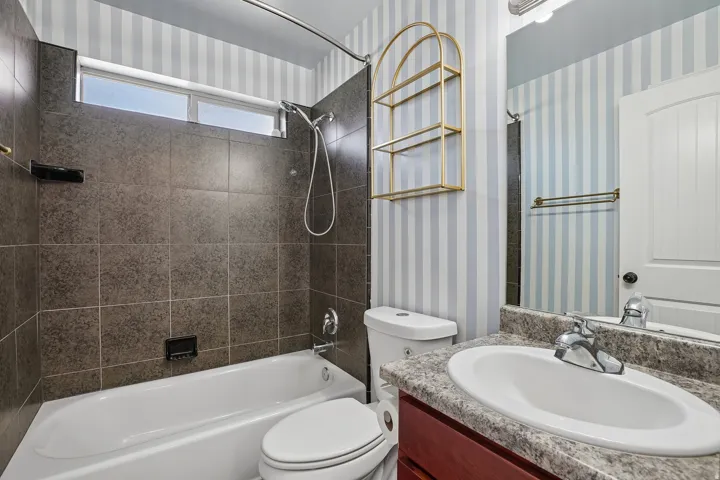 Built-in bathtub with dark stone-look tile surround, transom window, and a single vanity with a solid surface countertop