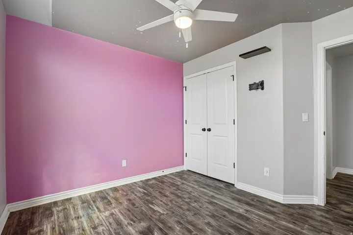 Wood-finish flooring, white bi-fold closet doors with black hardware, white ceiling fan with integrated lighting, and white trim