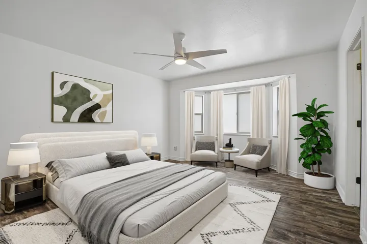 Bay window with multiple panels, ceiling fan with integrated lighting, wood-finish flooring, and white walls