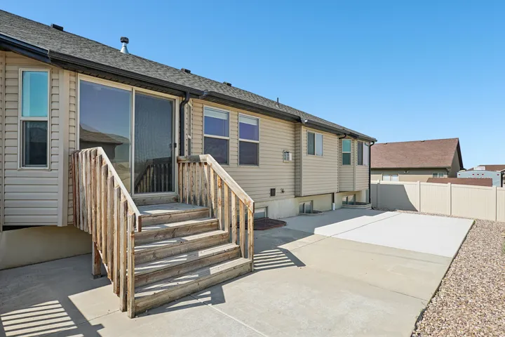 Sliding glass door access to a concrete patio, wood-finish stairs, and a gravel perimeter