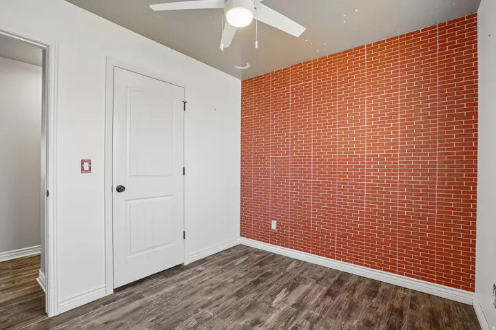 Wood-finish flooring, white paneled door, brick-pattern accent wall, and ceiling fan