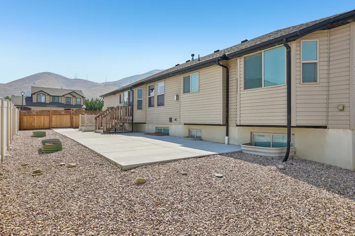 Rear exterior with light-toned siding, concrete patio, gravel landscaping, and a wooden fence