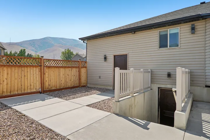 Siding exterior with a mountain backdrop, featuring a fenced perimeter, concrete walkway, and separate entry