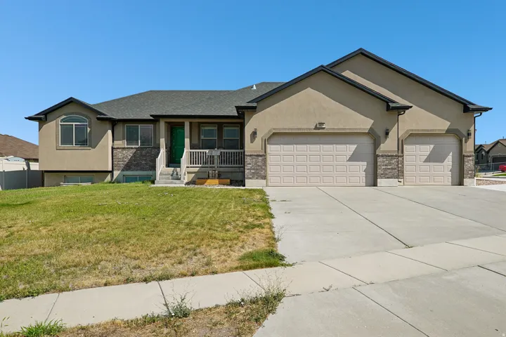 Spacious ranch-style home featuring a stucco exterior with architectural stone accents, dual three-car garages, a covered front porch with railings, and a manicured lawn with concrete driveway