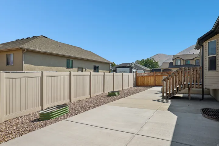 Paved concrete pathway with a durable privacy fence, gravel border, and a wooden staircase