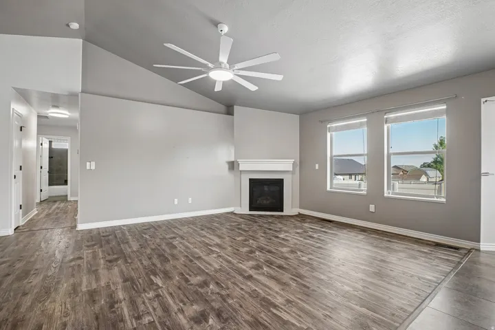 Spacious open-concept living area featuring wood-finish flooring, a fireplace with surround, recessed lighting, and a modern ceiling fan