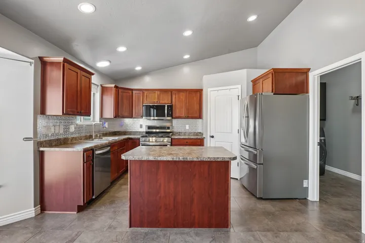 Chef's kitchen featuring rich wood cabinetry, stainless steel appliances, granite countertops, a large center island with seating, and recessed lighting throughout