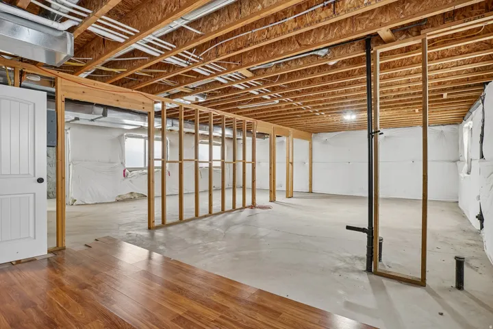Unfinished basement with exposed ceiling joists, framed interior walls, concrete flooring, and existing plumbing rough-ins