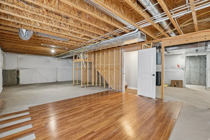 Unfinished basement featuring exposed wood joists, concrete flooring, and partial wood-finish flooring