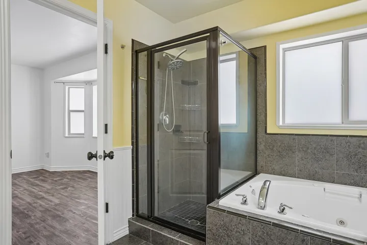 Enclosed shower with dark-framed glass, jetted soaking tub, tile surround, and privacy glass windows