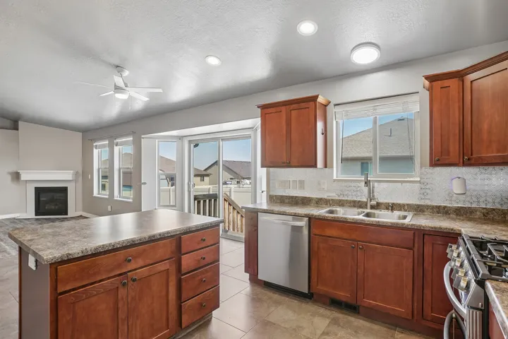 Kitchen island with storage, wood-finish cabinetry, stainless steel dishwasher, double basin sink, and mosaic tile backsplash