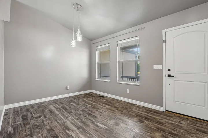 Bright, open room featuring wood-finish flooring, large windows with natural light, pendant lighting fixture, and a white six-panel entry door