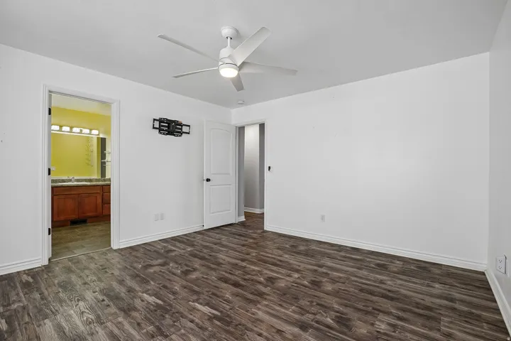 Wood-finish flooring throughout, white walls, and a white ceiling fan with integrated lighting