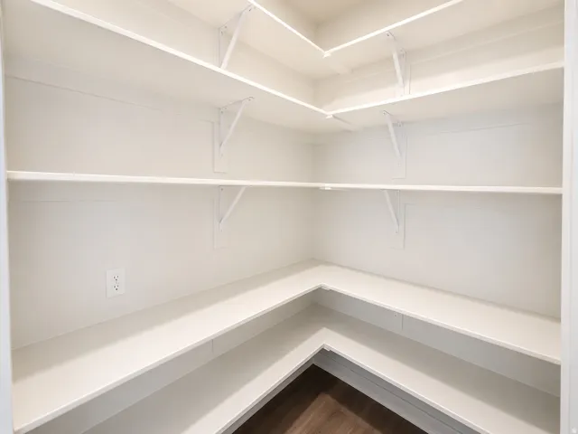 Walk-in pantry with extensive white shelving, integrated wall outlet, and wood-finish flooring