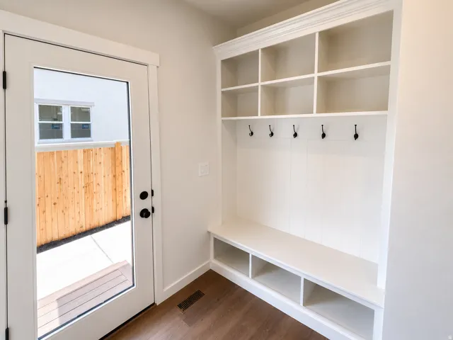 Built-in white storage unit with cubbies and hooks, wood-finish flooring, glass-paneled door, and a privacy fence