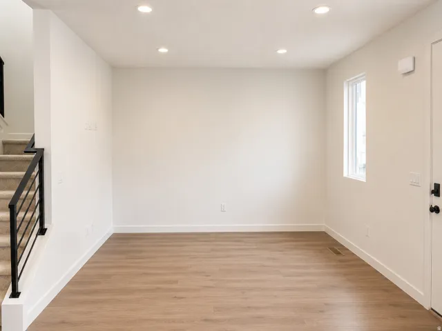 Recessed ceiling lighting, wood-finish flooring, white walls, white trim, and a window with white casing