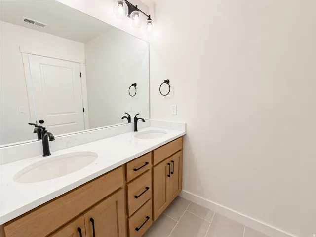 Double vanity with light wood-finish cabinetry, white countertops, and matte black fixtures