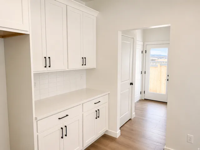 White shaker-style cabinetry with matte black hardware, light-toned countertop, subway tile backsplash, and wood-finish flooring