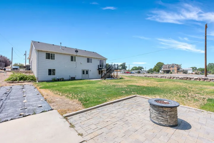 Spacious backyard featuring a paver patio with a stone-clad fire pit, an expansive lawn, and a two-story exterior with light-colored siding and multiple windows
