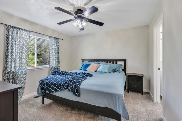 Bright interior owner's space featuring a window with curtains, a ceiling fan with integrated lighting, and neutral-toned walls