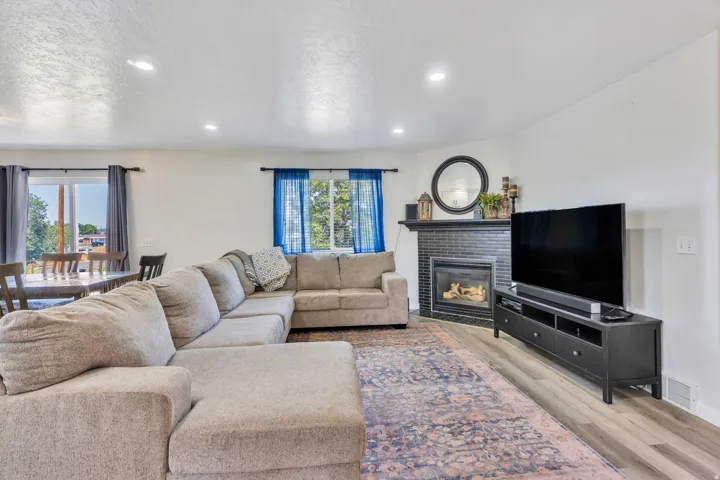 Spacious living room featuring a sectional seating arrangement, gas fireplace with black surround and mantel, flat-screen television mounted above media console, recessed ceiling lighting, and plush area rug