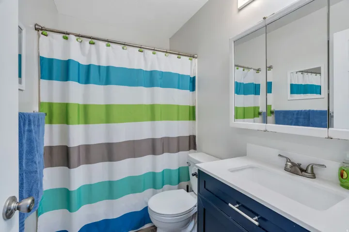 Hall bathroom featuring a navy blue vanity with a white countertop and integrated sink, a wall-mounted mirrored medicine cabinet, and a brushed nickel faucet