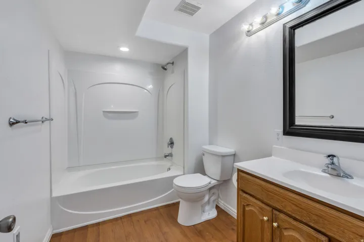Spacious full bathroom featuring a wood-finish vanity with integrated sink and ample countertop space, large framed mirror with integrated lighting, separate soaking tub with curved surround and tile enclosure, and ceramic floor