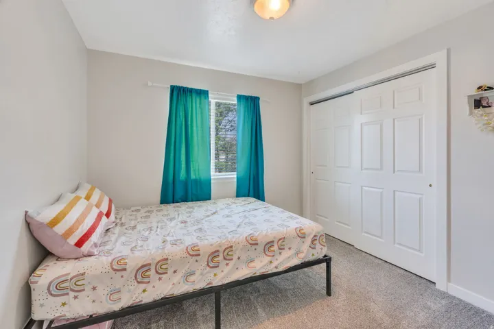 Comfortable bedroom featuring a metal bed frame, carpet flooring, and dual teal curtain panels framing a window