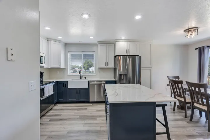 Kitchen featuring a large island with a patterned countertop, a white farmhouse sink, stainless steel appliances, and two-tone cabinetry