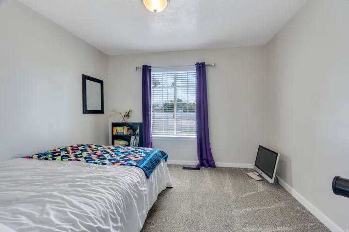 Bright bedroom featuring neutral carpeting, a large window with purple drapery hardware, recessed ceiling lighting, and ample natural light