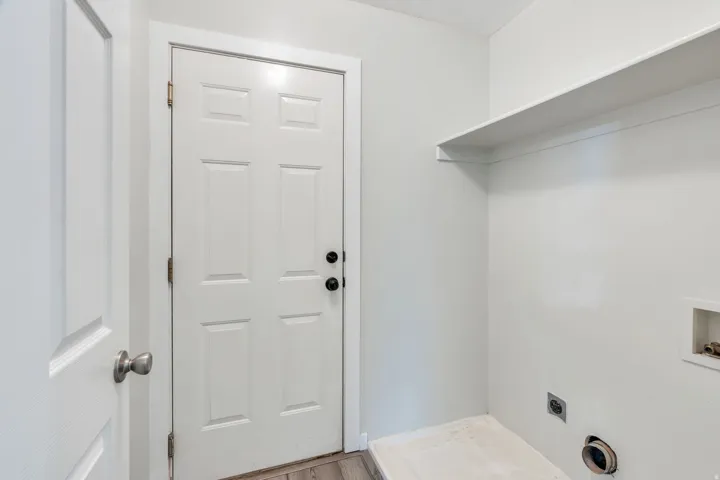 Dedicated laundry room featuring washer and dryer hookups, white six-panel entry door with satin nickel hardware, shelving for storage, and neutral wall finishes