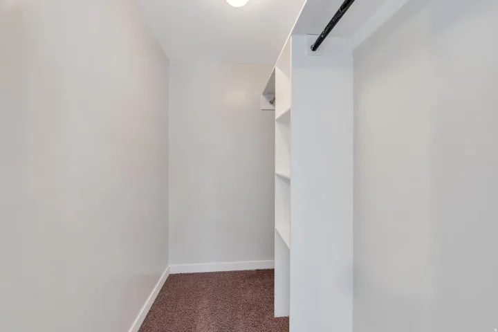 Spacious walk-in closet featuring clean white cabinetry with multiple shelving units, recessed lighting, and warm wood-finish flooring
