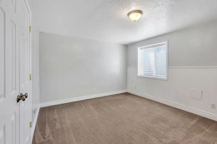 Spacious bedroom offering neutral wall finishes, carpeted flooring, a large window with blinds providing natural light, and a closet with bi-fold doors