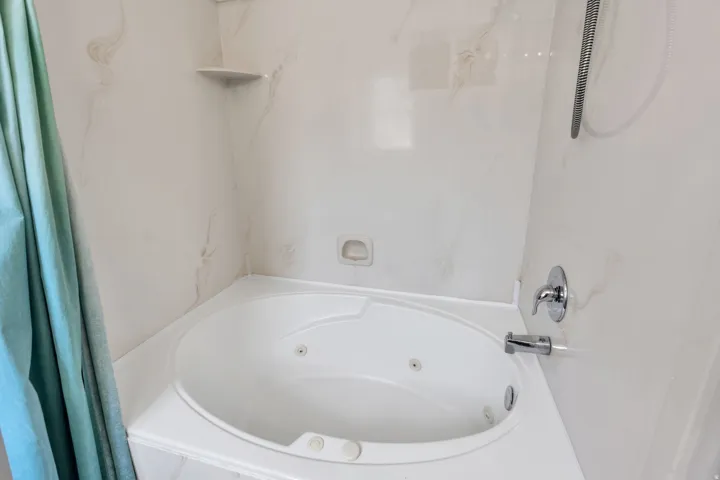 White jetted corner bathtub in the master with integrated shelving, chrome fixtures, and a shower sprayer