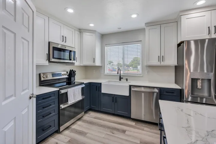 Modern kitchen featuring white shaker cabinetry, stainless steel appliances including a French-door refrigerator and dishwasher, and a ceramic farmhouse sink with chrome faucet