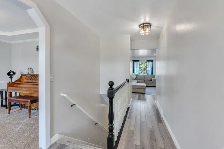 Elegant hallway featuring gleaming wood-finish flooring, crisp white walls with architectural molding, and a black wrought-iron stair railing with turned balusters