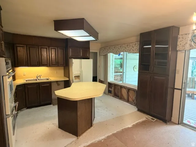 Open-concept kitchen featuring dark wood cabinetry, a central island with a light-toned countertop, and a double basin sink.