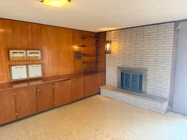 Wood-paneled wall with extensive built-in cabinetry, integrated shelving, and a brick  gas fireplace.