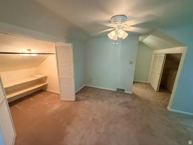 Carpeted  home offic with a ceiling fan, sloped ceiling details, and two built-in closet spaces featuring louvered bi-fold doors.