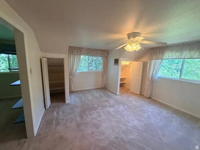 Spacious upstairs bedroom with plush carpeting, two large windows, a built-in closet with shelving, and a ceiling fan with integrated lighting,