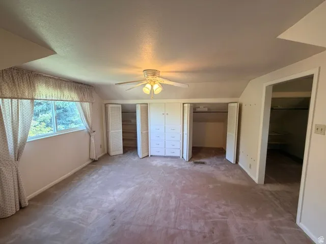 Spacious upstairs bedroom featuring sloped ceilings, a wide window, ceiling fan with integrated lighting, built-in cabinetry with drawers, and two bi-fold door closets.