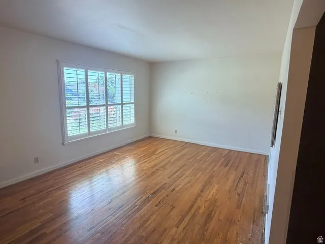 Living room featuring hardwood flooring, a large window with white plantation shutters, white baseboards, and light-colored walls.