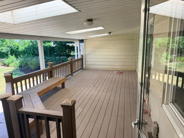 Covered deck featuring composite wood-finish flooring, wood railings, and a built-in bench.
