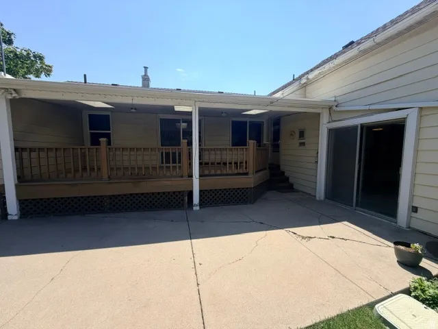 Rear exterior featuring a covered deck, a sliding glass door to family room, and a stairway to backyard with large concrete patio.