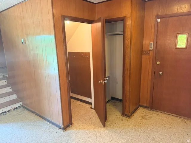 Entryway from front of house featuring wood paneling, a wood-finish door with a frosted glass insert, and a built-in closet and crawl space.