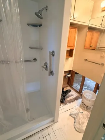 3/4 bath with white shower enclosure featuring a multi-function showerhead, integrated shelving, and grab bars and adjoining sink and toilet connections.