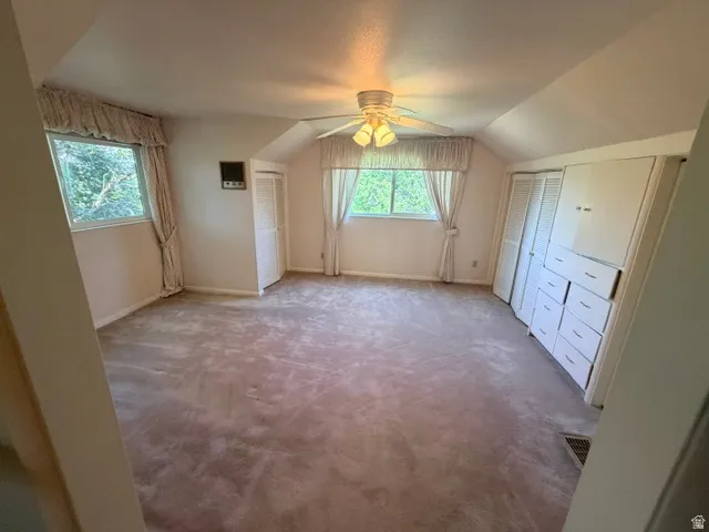 Upstairs bedroom featuring a ceiling fan with integrated lighting, multiple windows, and built-in cabinetry with drawers.