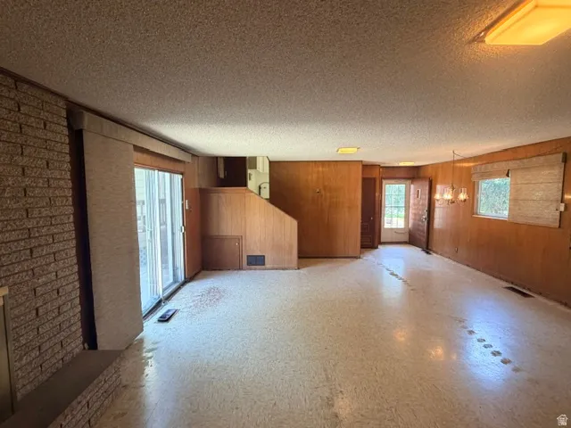 What a great space for home entertaining!!!! Spacious interior featuring wood paneling, a brick-faced gas fireplace, a large sliding glass door, multiple windows, and overhead lighting.