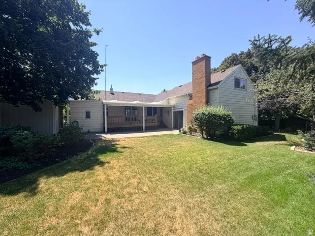 Charming ranch-style home with brick chimney and siding exterior, featuring a spacious rear yard with mature landscaping and established trees.