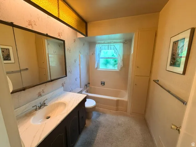 Bathroom featuring a single vanity with a white countertop and integrated sink, a medicine cabinet mirror, a bathtub with a shower, a toilet, and built-in vertical storage cabinetry.
